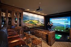 a man is playing a video golf game on the large screen in his home office