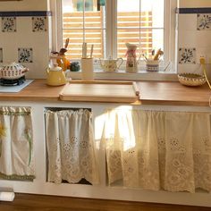 a kitchen with white cabinets and wooden counter tops next to a window filled with sun shining through the blinds