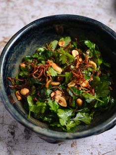 a bowl filled with greens and nuts on top of a table