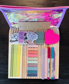 the contents of a craft kit in a plastic bag on a wooden table with pens and markers