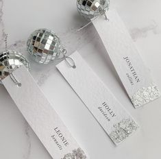 three silver disco ball necklaces with name tags attached to them on a marble surface