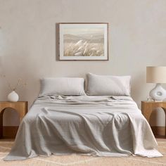 a bed with white sheets and pillows in a neutral colored room, next to two nightstands