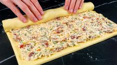 two hands are placing toppings on top of a homemade pizza dough sheet that's ready to go into the oven