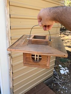 a hand is holding a birdhouse that has a clock on it