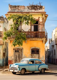 an old blue car parked in front of a yellow and brown building with balconies