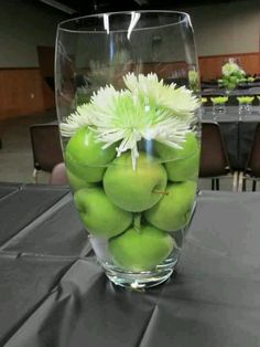 a glass vase filled with green apples on top of a black tablecloth covered table