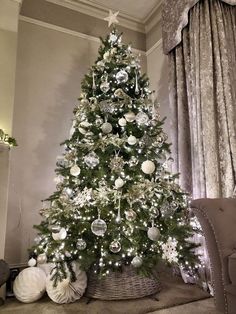 a decorated christmas tree in a living room with white and silver ornaments on the top