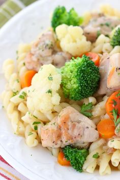 a white plate topped with pasta and meat covered in broccoli, carrots and cauliflower