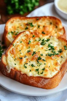 two pieces of bread with cheese and parsley on top sitting on a white plate