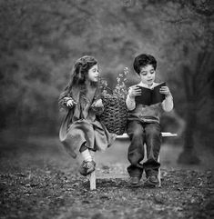 two children are sitting on a bench reading books and holding flowers in their hands,