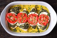 a casserole dish with tomatoes, spinach and cheese in it on a wooden table