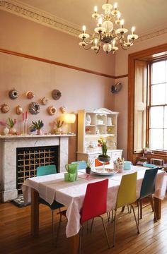 a dining room table with colorful chairs and plates on the wall next to a fireplace