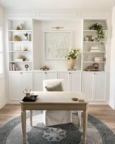 a wooden table topped with white vases filled with flowers and plants next to bookshelves