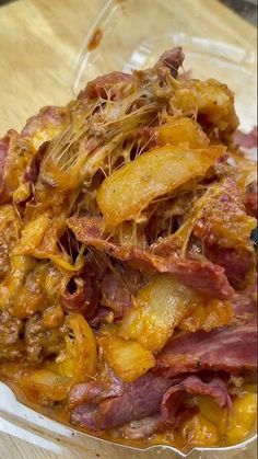 a bowl filled with meat and potatoes on top of a wooden table next to a fork