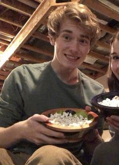 two people are holding plates of food in their hands and smiling at the camera while sitting down