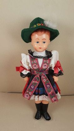 a small doll wearing a green hat and dress with red trimmings on it's chest