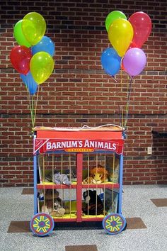 an animal cage with balloons and stuffed animals in it on the floor next to a brick wall