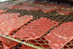 raw meat sitting on top of a metal grate covered in red sauce and seasoning