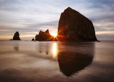 the sun is setting behind two large rocks in the ocean with reflections on the water