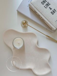 a white candle holder sitting on top of a table next to a book and a pen