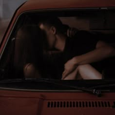 a man and woman kissing in the back seat of a red car at night time