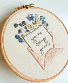 a close up of a embroidery on a white surface with a wooden frame and some flowers