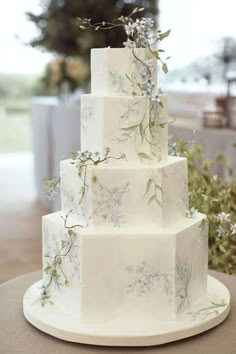 a three tiered white cake with blue flowers and greenery on the top layer