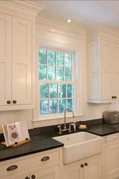 a kitchen with white cabinets and black counter tops is pictured in this image, there are two windows above the sink