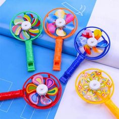 four colorful plastic hand fans sitting on top of a blue book next to each other