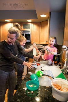 a group of people standing around a kitchen counter with food in bowls and utensils