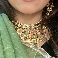 a close up of a woman wearing a green and gold necklace with pearls on it