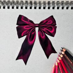 a pink bow on top of a notebook next to colored pencils