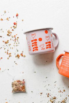 an orange and white coffee mug next to a bag of granola