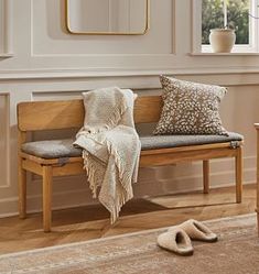 a wooden bench sitting in front of a window next to a table with a mirror on it