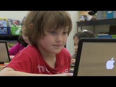 a young boy sitting in front of a laptop computer with another child behind him looking at the screen