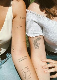 two women with matching tattoos on their arms sitting next to each other in the grass