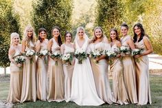 a group of women standing next to each other in front of trees and bushes with bouquets