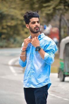 a man is walking down the street with his hand on his chest and wearing a blue shirt