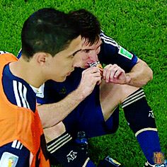 two soccer players are sitting on the grass eating something out of their mouths while looking at each other