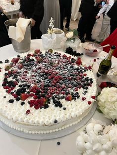 a white cake with berries and blueberries on it sitting on top of a table