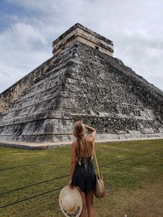 a woman standing in front of an ancient pyramid with a straw hat on her head