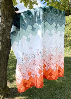 an orange and white quilt hanging from a tree