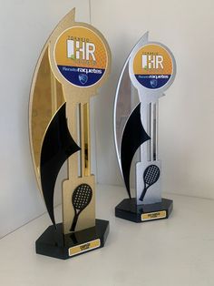 two trophies with tennis rackets on them sitting next to each other in front of a white wall