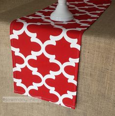 a red and white table runner on top of a beige couch with a candle holder