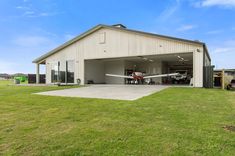 an airplane is parked in the garage of a house with grass and other vehicles nearby