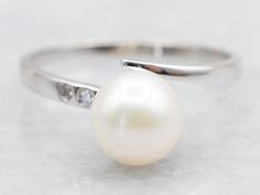 Anchor your style with this alluring bypass ring! Adorned with dazzling diamonds and a lustrous pearl, it's the living embodiment of timeless beauty. Plus, it's forged from white 18-karat gold to ensure durability that'll last for years to come! Metal: 18K White Gold Gem: Pearl Gem Measurements: 7.1 mm, Round Accents: 2 Diamonds totaling .03 Carats, H-I in Color, I in Clarity Ring Size: 6.75 Marks: "G18K" Stamped on the inside band SKU #: A50162 Each piece has been identified and graded by a Graduate Gemologist who has been certified by the Gemological Institute of America (GIA). We have six brick-and-mortar storefronts in Maine, Massachusetts, and New Hampshire and have been in business for over 25 years! Please visit our Shop's About Page or our website for more information about our jew White Gold Pearl Ring, Pearl Ring Vintage, Vintage Pearl Ring, Pearl Rings Vintage, Ring Pearl, Gold Pearl Ring, Pearl And Diamond Ring, Bypass Ring, Ring White Gold