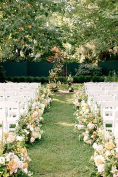 an outdoor ceremony setup with white chairs and flowers on the aisle, surrounded by greenery