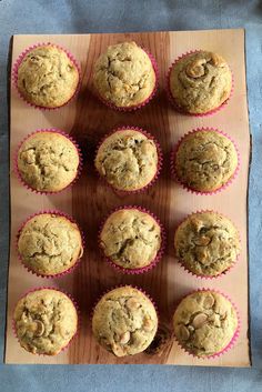 twelve muffins on a wooden board with pink paper wrappers around them, ready to be eaten