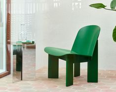 a green chair sitting in front of a mirror next to a vase with a plant