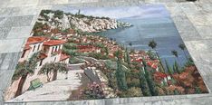 an area rug on the ground with a painting of a town by the sea and trees